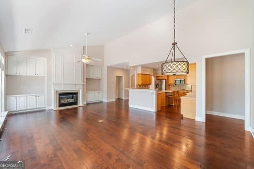 1330 Badingham Dr, Cumming, GA 30041 - unfurnished living room featuring high vaulted ceiling, dark wood-type flooring, a ceiling fan, radiator, and a glass covered fireplace