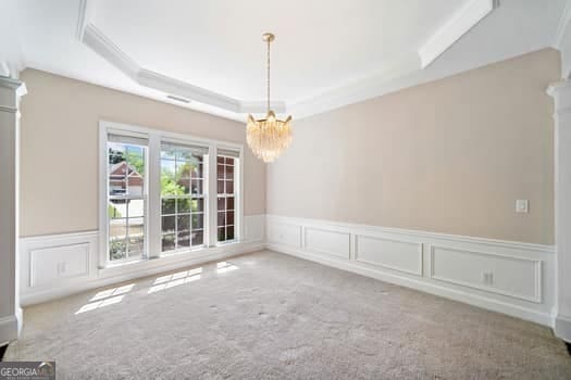 1330 Badingham Dr, Cumming, GA 30041 - carpeted empty room featuring a raised ceiling, a chandelier, a decorative wall, and a wainscoted wall