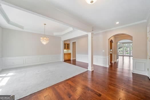 1330 Badingham Dr, Cumming, GA 30041 - empty room with arched walkways, a chandelier, decorative columns, a decorative wall, and wood finished floors