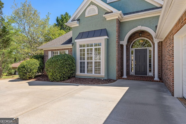 doorway to property with a standing seam roof, stucco siding, metal roof, and brick siding