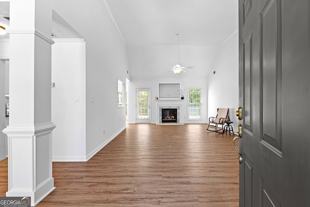 living room featuring decorative columns, light wood-type flooring, a ceiling fan, a glass covered fireplace, and baseboards
