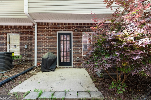 property entrance with a patio area, central AC unit, and brick siding
