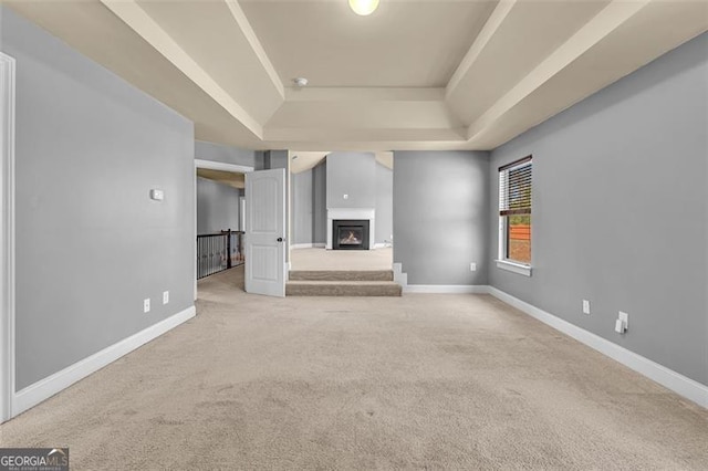 unfurnished living room with carpet flooring, baseboards, a lit fireplace, and a raised ceiling