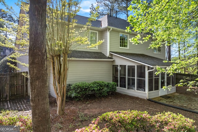 back of property with fence, a sunroom, and a shingled roof