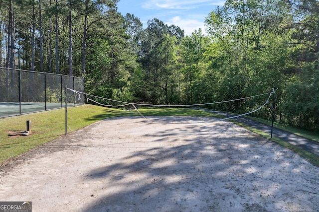 view of home's community featuring a view of trees, fence, and volleyball court