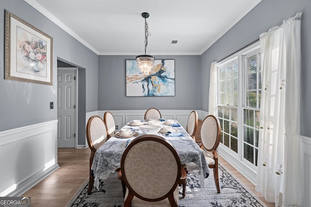 dining area with wainscoting, a notable chandelier, ornamental molding, and light wood-style flooring