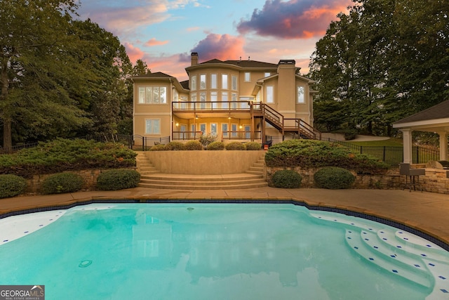 12 Arbor Shrs, Newnan, GA 30265 - back of property at dusk featuring stairs, a chimney, a balcony, stucco siding, and an outdoor pool