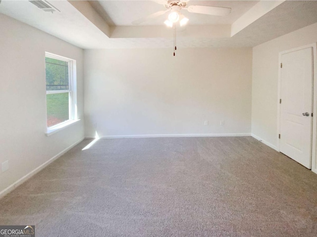 spare room with a tray ceiling, carpet flooring, ceiling fan, and visible vents