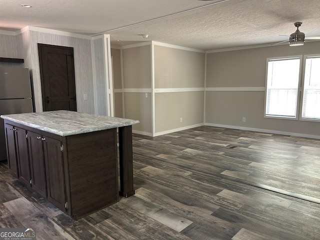 kitchen with a textured ceiling, dark wood-style flooring, dark brown cabinets, freestanding refrigerator, and ornamental molding