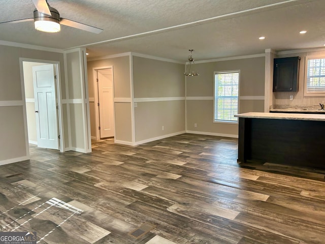 unfurnished living room with ceiling fan with notable chandelier, dark wood finished floors, baseboards, ornamental molding, and recessed lighting