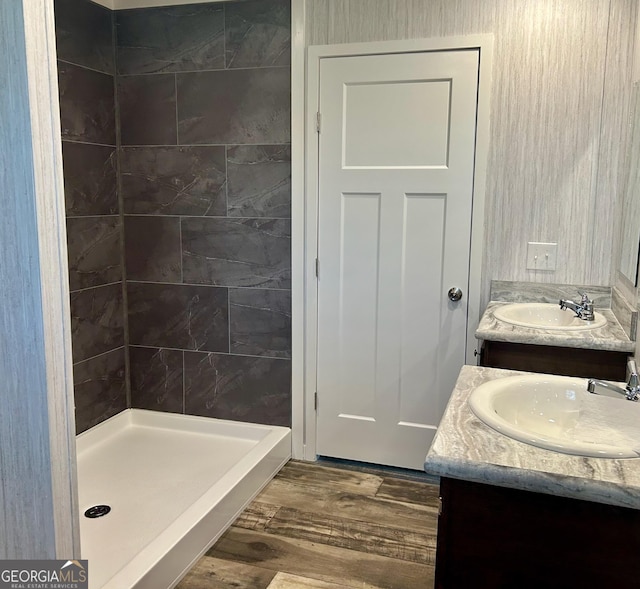 bathroom with wood finished floors, a sink, double vanity, and a stall shower