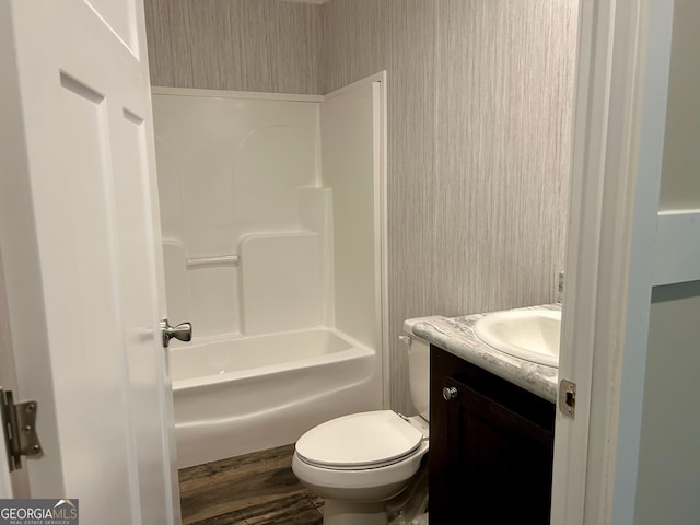 full bathroom with toilet, wallpapered walls, wood finished floors, washtub / shower combination, and vanity
