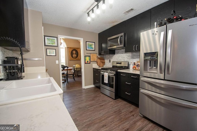 kitchen featuring dark cabinets, decorative backsplash, appliances with stainless steel finishes, and visible vents