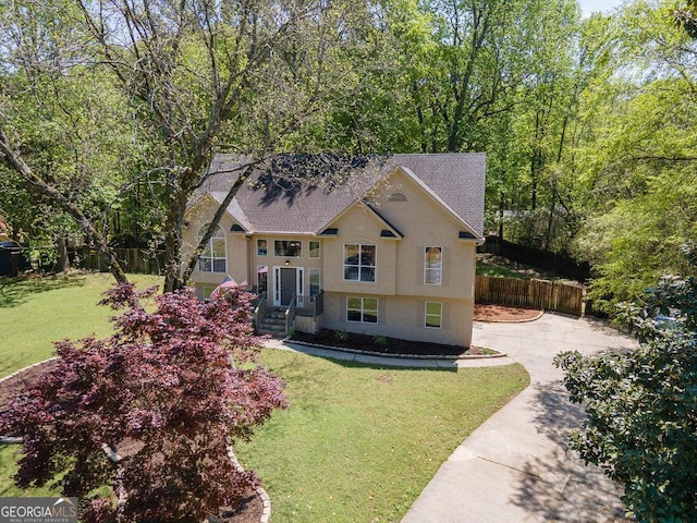 bi-level home featuring fence, a shingled roof, concrete driveway, stucco siding, and a front yard
