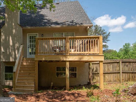 rear view of house featuring a wooden deck, stairs, a chimney, roof with shingles, and fence