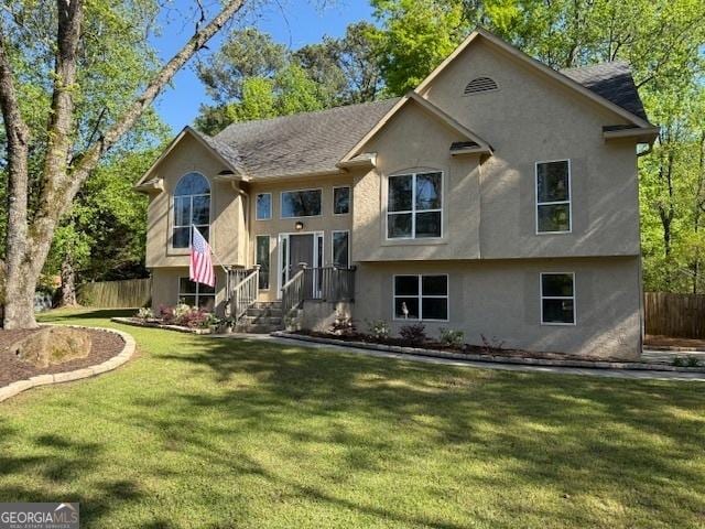 raised ranch featuring stucco siding, fence, and a front yard