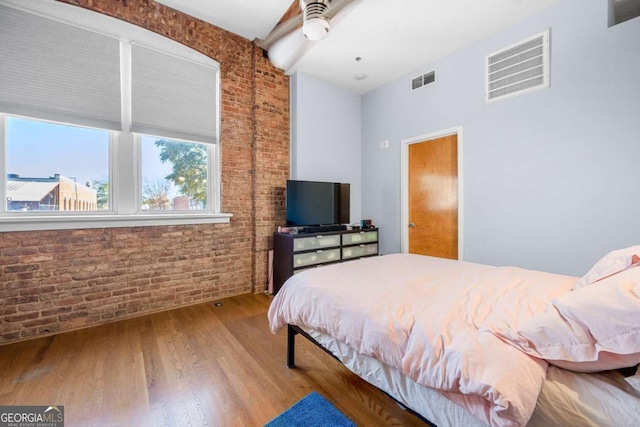 bedroom featuring brick wall, visible vents, a ceiling fan, and wood finished floors