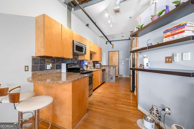 kitchen with light wood-style floors, open shelves, appliances with stainless steel finishes, decorative backsplash, and a breakfast bar area