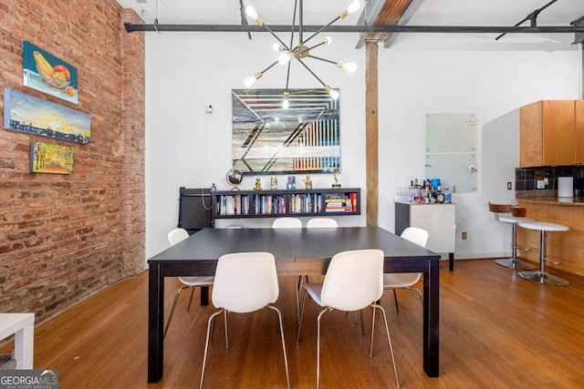 dining room featuring wood finished floors, a towering ceiling, an inviting chandelier, and brick wall