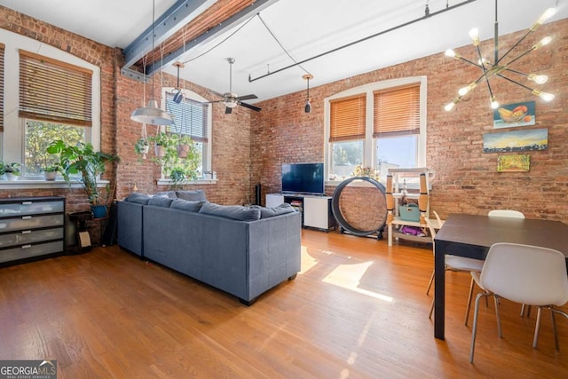 living area with brick wall, a towering ceiling, ceiling fan with notable chandelier, and wood finished floors