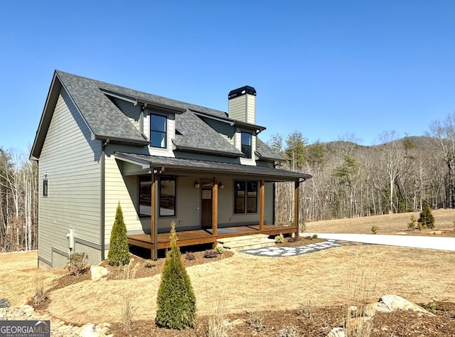 view of front facade featuring a porch, roof with shingles, and a chimney