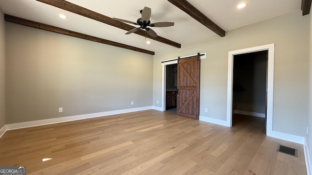 unfurnished bedroom with beamed ceiling, a spacious closet, visible vents, a barn door, and baseboards