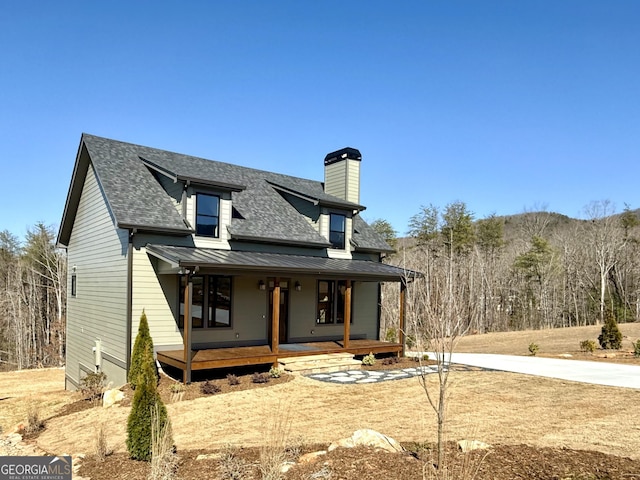 back of house with a standing seam roof, covered porch, roof with shingles, metal roof, and a chimney