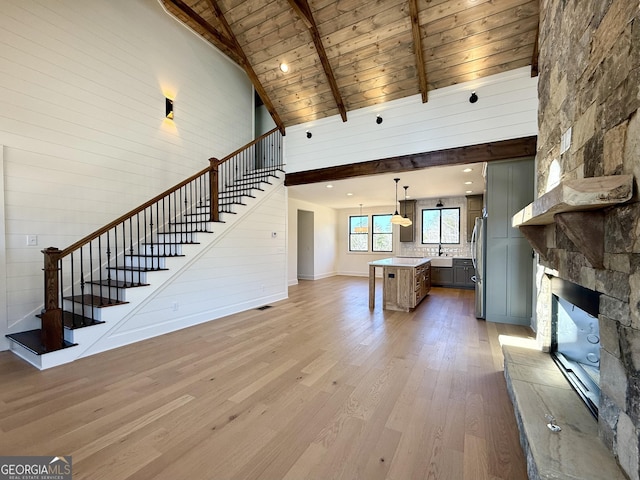 unfurnished living room with a stone fireplace, light wood-type flooring, stairway, beam ceiling, and high vaulted ceiling