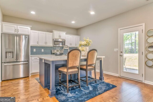 1302 Gardenia Ct, Villa Rica, GA 30180 - kitchen with a kitchen bar, tasteful backsplash, light wood-type flooring, white cabinets, and appliances with stainless steel finishes