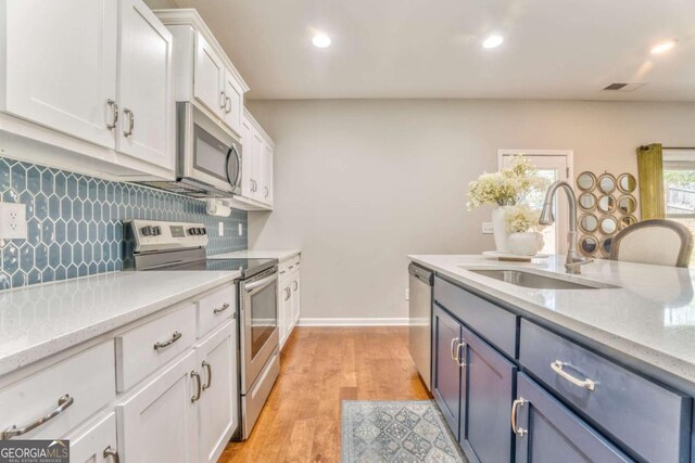 1302 Gardenia Ct, Villa Rica, GA 30180 - kitchen with white cabinets, a sink, light wood finished floors, stainless steel appliances, and decorative backsplash