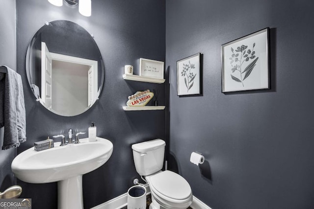 half bath featuring baseboards and toilet