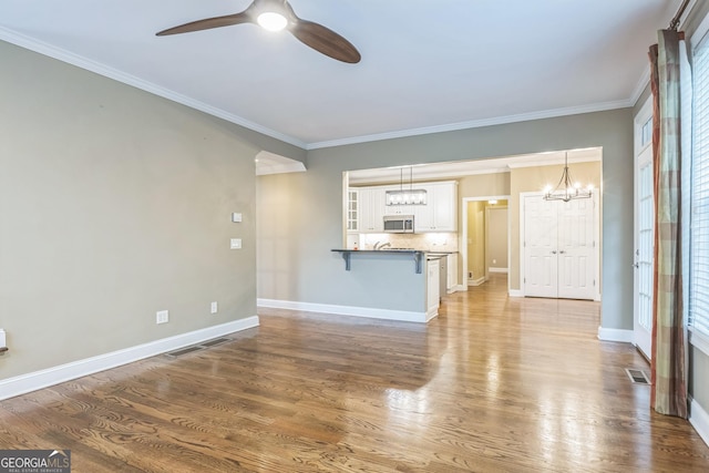 unfurnished living room featuring visible vents, wood finished floors, ceiling fan with notable chandelier, and crown molding