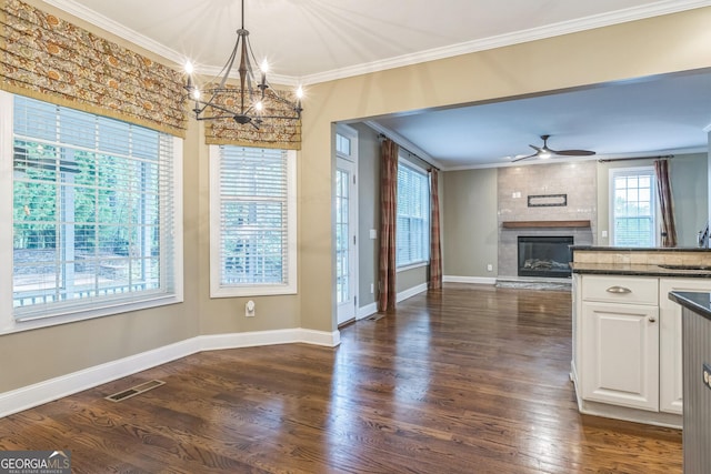 unfurnished dining area featuring a large fireplace, visible vents, crown molding, and ceiling fan with notable chandelier