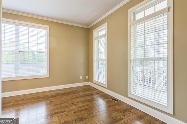 empty room featuring visible vents, crown molding, dark wood finished floors, and baseboards
