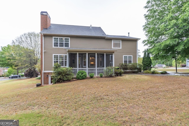 back of house with a chimney, a sunroom, and a lawn