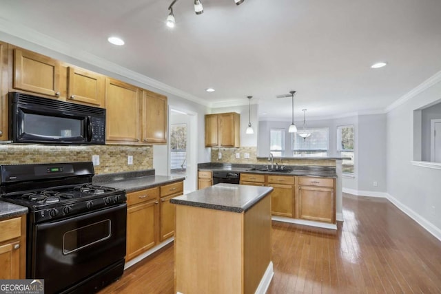 kitchen with a peninsula, dark countertops, black appliances, decorative backsplash, and a sink