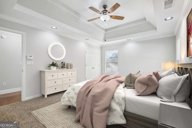 carpeted bedroom featuring a raised ceiling, baseboards, visible vents, and recessed lighting
