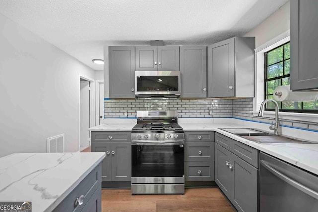 kitchen with a sink, tasteful backsplash, visible vents, gray cabinetry, and appliances with stainless steel finishes