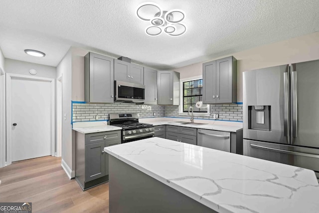 kitchen with light wood finished floors, stainless steel appliances, a sink, light stone counters, and gray cabinets