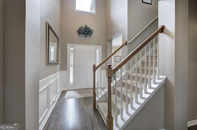 foyer entrance featuring stairway, a high ceiling, a wainscoted wall, a decorative wall, and wood finished floors