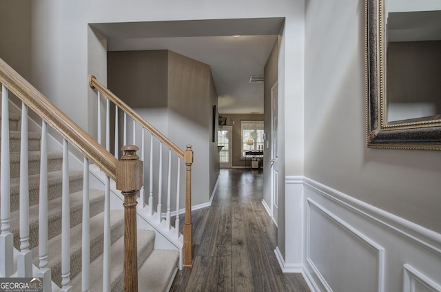 hall with dark wood-style flooring, visible vents, a wainscoted wall, and stairway