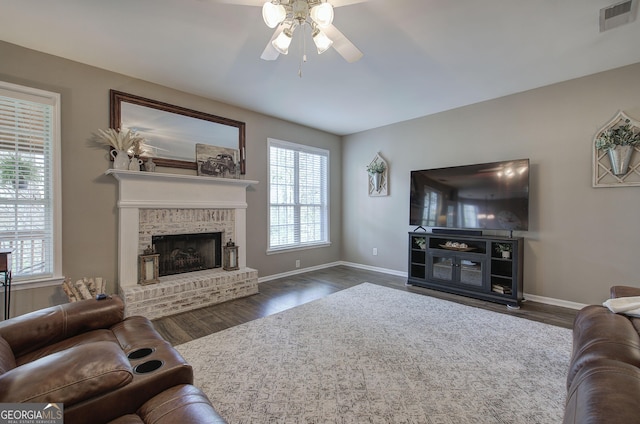 living room featuring visible vents, baseboards, ceiling fan, a fireplace, and wood finished floors