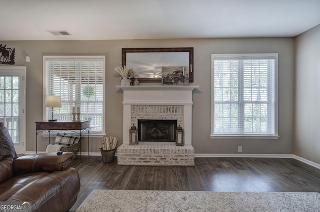 living room with visible vents, baseboards, a brick fireplace, and dark wood-style floors