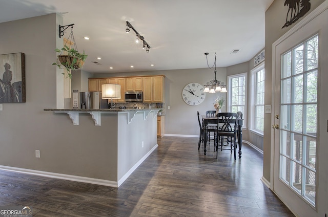 kitchen featuring a kitchen breakfast bar, baseboards, dark stone countertops, dark wood finished floors, and appliances with stainless steel finishes