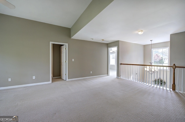spare room featuring light colored carpet, baseboards, and a notable chandelier
