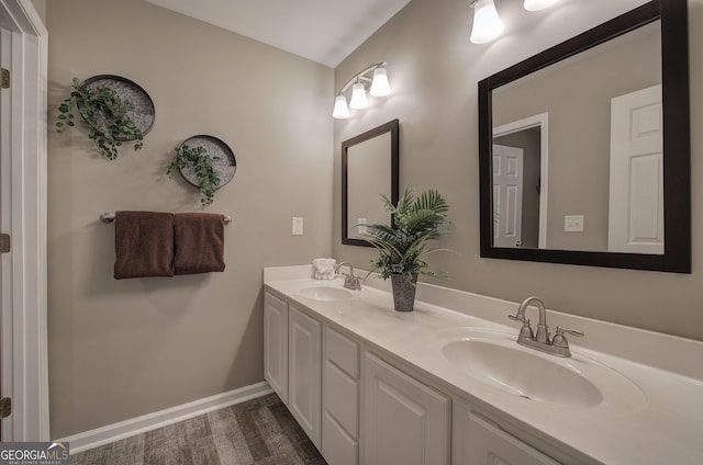 full bathroom with wood finished floors, double vanity, a sink, and baseboards