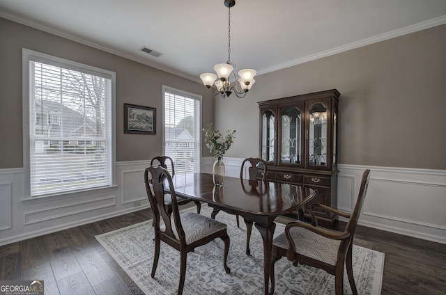 dining space with an inviting chandelier, ornamental molding, visible vents, a wainscoted wall, and dark wood-style flooring
