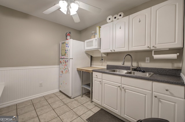 kitchen with white appliances, dark countertops, white cabinets, wainscoting, and a sink