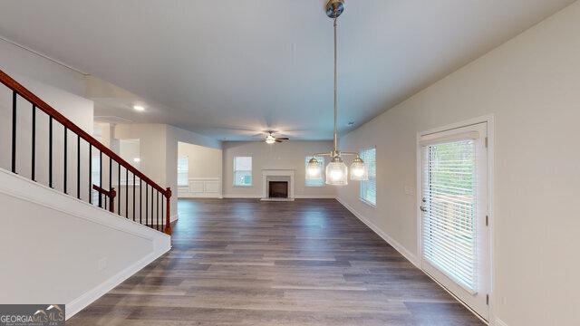 unfurnished living room with a ceiling fan, a fireplace with raised hearth, wood finished floors, stairs, and baseboards