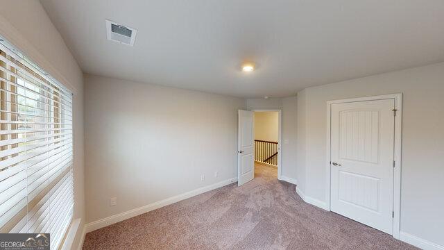 unfurnished bedroom with carpet flooring, visible vents, multiple windows, and baseboards